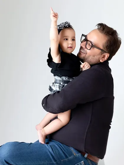 A father holds his baby girl, who points up with curiosity, creating a fun and interactive father-daughter portrait.