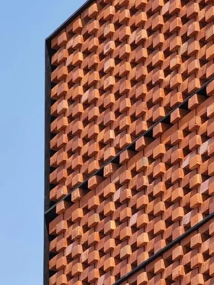 A close up of the 'Ishtika' brick facade against a clear blue sky. The rotated bricks create a highly textured, dynamic surface that changes with the light throughout the day.
