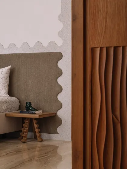 A detail of the guest bedroom, showing the carved wooden door and the playful, wavy edge of the upholstered headboard.