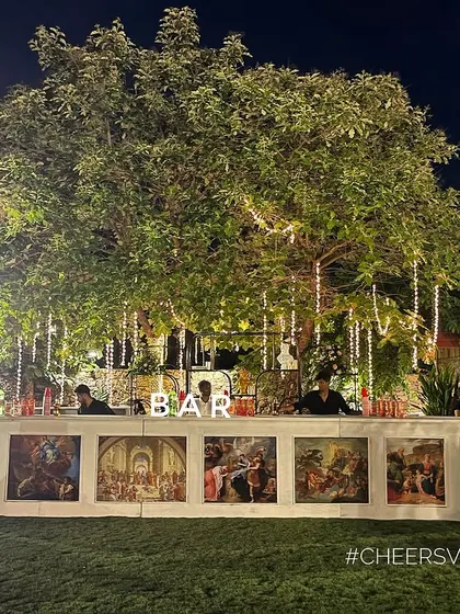 We created a grand, artistic bar for this lawn event. The counter features classic European art panels, flanked by stately pillars and set under a beautifully lit tree, making it a true statement piece.