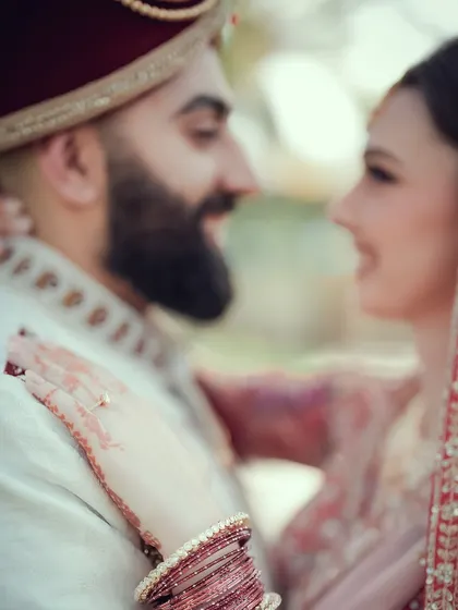 A soft-focus shot of a multicultural couple, with the focus on the bride's henna-adorned hand and wedding ring.