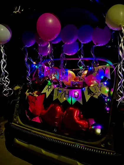 A car boot surprise decoration at night. The colorful fairy lights and balloons create a festive glow, perfect for a nighttime reveal.