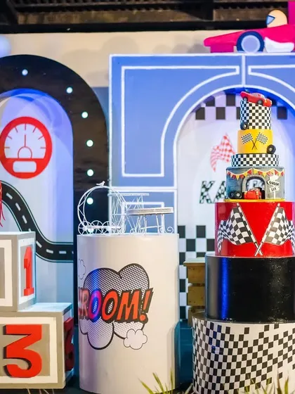 A close-up of the race car themed cake table, featuring a multi-tiered cake, "VROOM!" signs, and checkered flag details. The setup is bold, graphic, and full of energy.