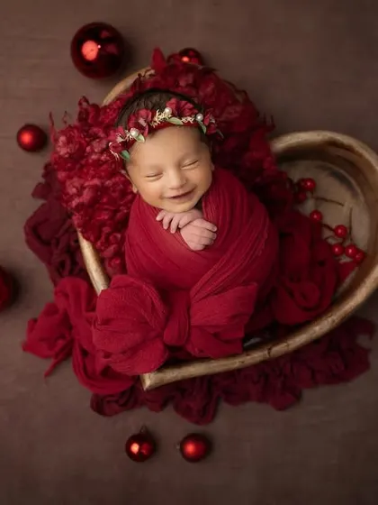 A beautiful smile from a newborn nestled in a heart shaped bowl, surrounded by festive red ornaments. This is the perfect way to celebrate your baby's first holiday season.