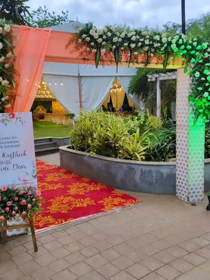 An elegant floral archway at the entrance to an outdoor event, complemented by a welcome sign and a traditional red carpet.