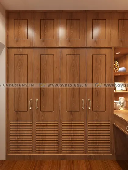 This classic wardrobe design features a rich teakwood finish with louvered details for ventilation. The unit is paired with an open dressing table area with its own storage and lighting, creating a complete and elegant personal care station.