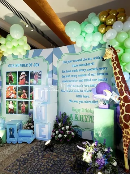 A photo wall for a carnival party, featuring a giraffe prop, pastel balloon garlands, and a personalized 'Our Bundle of Joy' message board.
