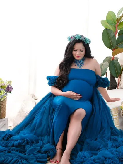 Seated gracefully on the edge of a daybed, this mother-to-be looks peaceful in a deep blue tulle gown. The floral crown and surrounding props add to the enchanting, garden-like feel of the portrait.