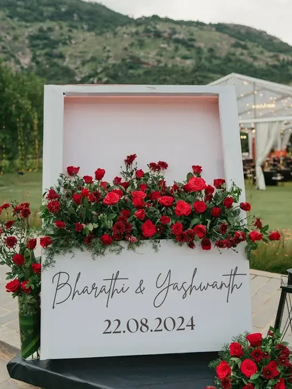 A modern welcome sign for a wedding, framed with a bed of vibrant red roses.