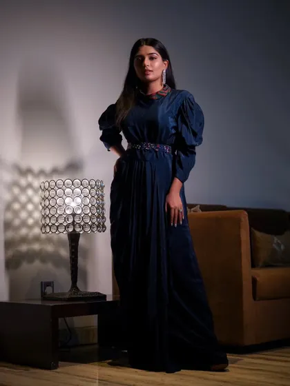 A full-length shot from the "Saphir" series, showing the entire elegant blue gown and the moody lighting of the room.