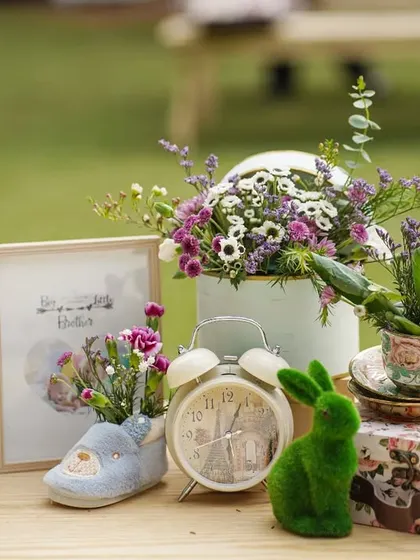 A collection of whimsical props on a table, including picture frames, a baby shoe filled with flowers, and mossy green rabbits.