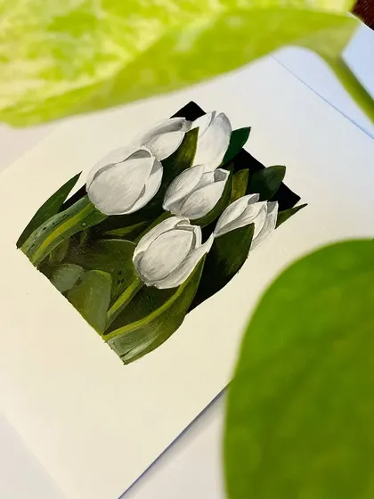 The white tulips painting nestled next to a plant.