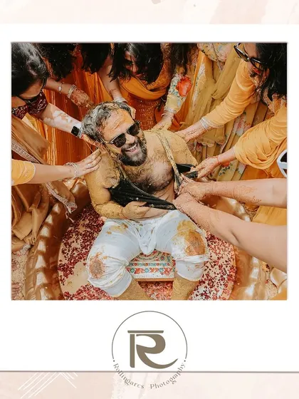 A fun, candid moment from a Haldi ceremony, framed as a polaroid. The groom is all smiles as his family and friends apply turmeric.