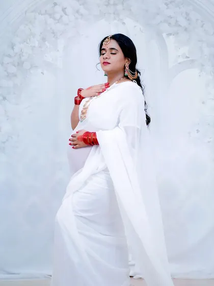 An ethereal and graceful pose from a creative maternity shoot. The makeup is soft and luminous, complementing the all-white theme and creating a truly angelic look.