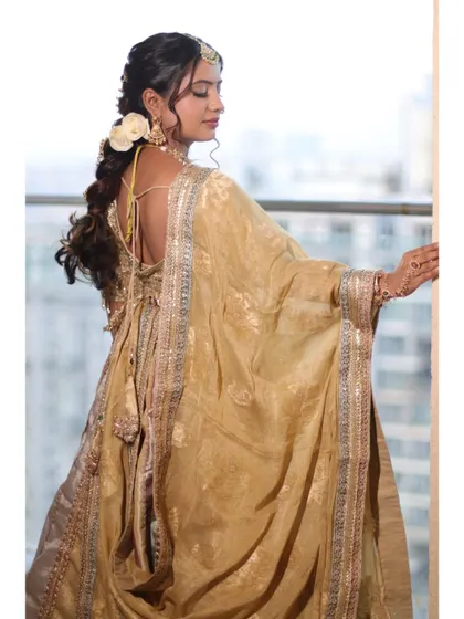 A view of the intricate hairstyle and the back of her stunning outfit. The white rose adds a touch of fresh, natural beauty.