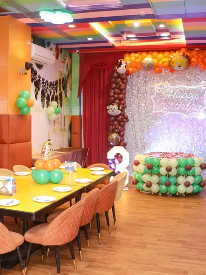 A view of a jungle-themed birthday setup, showcasing the balloon decor, cake table, and dining arrangement in the private party area.