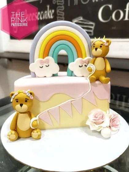 A delightful cake featuring two fondant teddy bears, a pastel rainbow, and fluffy fondant clouds. This design is perfect for a baby shower or a young child's birthday.