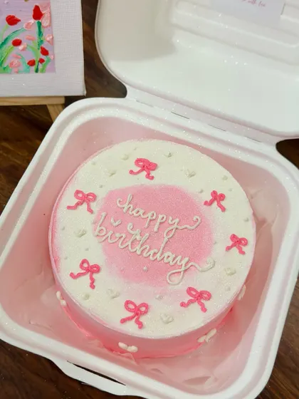 A lovely pink bento cake with an airbrushed center and delicate bow details. This coquette-style cake is perfect for a sweet and feminine celebration.