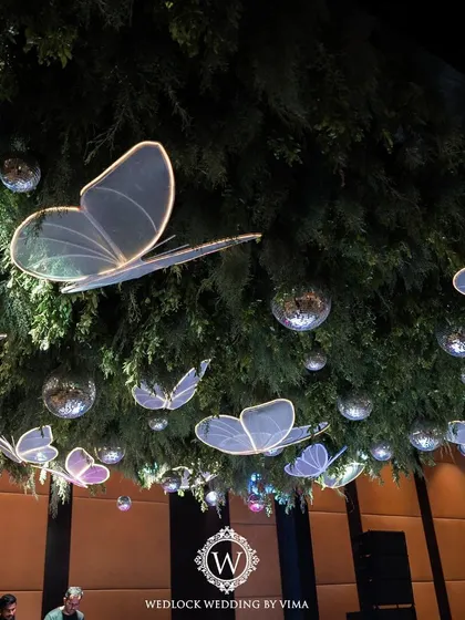 A walkthrough of a sangeet with an enchanted forest theme. The decor features a ceiling of lush greenery, sparkling disco balls, and glowing LED butterflies, creating a truly magical atmosphere.