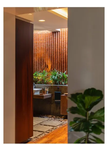 A glimpse into the open-air bathroom, where a wall of textured terracotta bricks and lush plants create a sanctuary for relaxation.