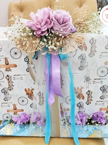 This image shows the scale of our gift wrapping services. A large gift is wrapped in quirky, fun paper and adorned with a cascade of purple and blue ribbons and flowers.
