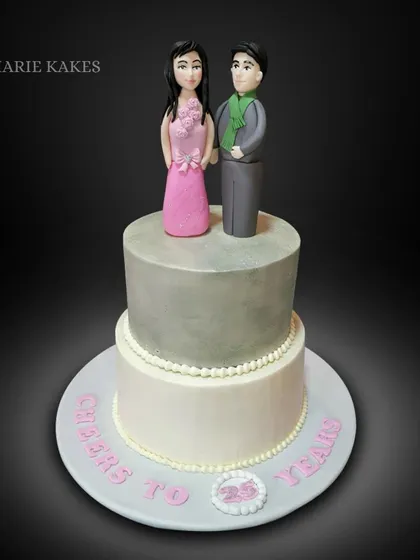 Celebrating 25 years of love with this special anniversary cake. It's a two-tiered design with a silver-grey finish, topped with custom fondant figures of the couple.