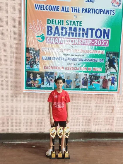Prasidhi Gupta standing proudly with her three trophies, a triple-crown achievement at the Delhi State Badminton Championship 2022.