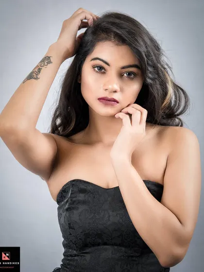 A confident portrait where the model looks directly at the camera. Her hand runs through her hair, showing off an arm tattoo and an unapologetic attitude.