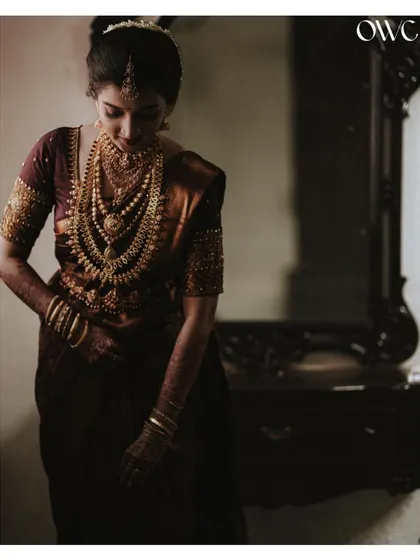 A pensive and beautiful portrait of the bride looking down, highlighting the details of her saree and jewellery.