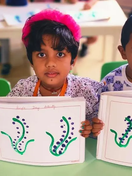 Two students show their completed finger paintings, showcasing their artistic talent.