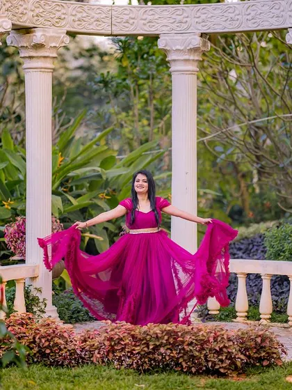 A joyful portrait in the garden. The bride-to-be shows off her magenta gown against the white pillars, creating a vibrant and happy pre-wedding photo.