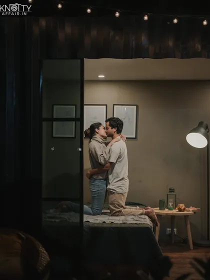 A romantic kiss in a softly lit bedroom. The framing through the doorway creates a sense of looking in on a private, intimate moment.