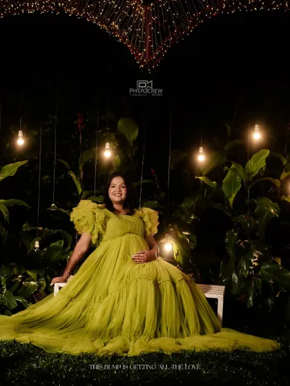 A showcase of our creative night-time maternity shoots. Here, Deepa is seated in a lush garden setting, illuminated by hanging bulbs and a heart-shaped light installation, creating a truly magical and romantic atmosphere.