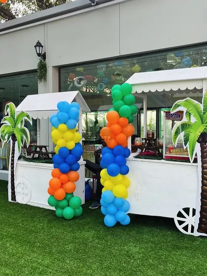 Food carts decorated with colorful balloon columns and palm tree cutouts, adding to the tropical party atmosphere.