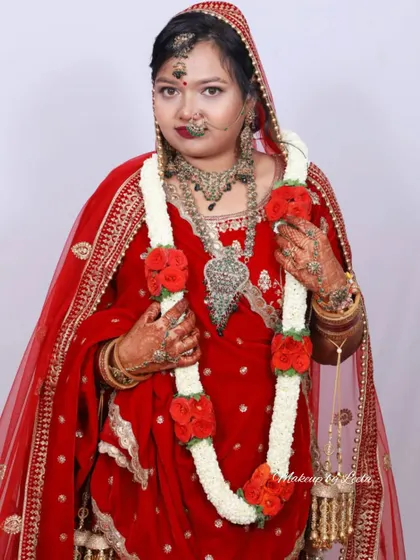 A close-up of a North Indian bride. Her look includes heavy traditional jewelry and a red veil (dupatta), with makeup that highlights her eyes and lips.