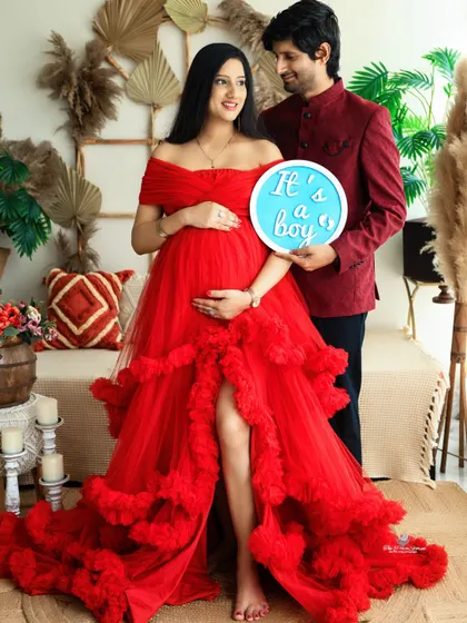 A proud moment for the dad-to-be as he holds the "It's a boy" sign. The couple stands together in coordinated red and maroon outfits, radiating joy.