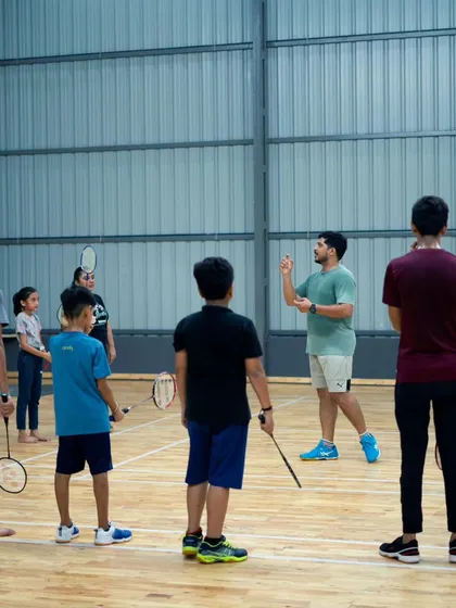 A group of adult learners listening to their coach at Oneiros Sports Club. Our classes combine instruction with plenty of on-court practice.