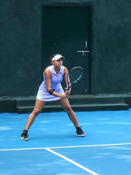 A player in a low, ready stance, preparing to return a serve. This fundamental position is drilled relentlessly to ensure our players are prepared for every point.