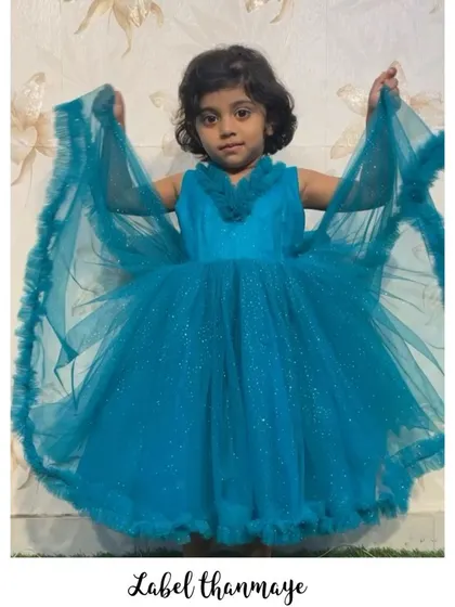 This little girl is showing off her blue frills frock, which has a sparkly fabric and a ruffled neckline.
