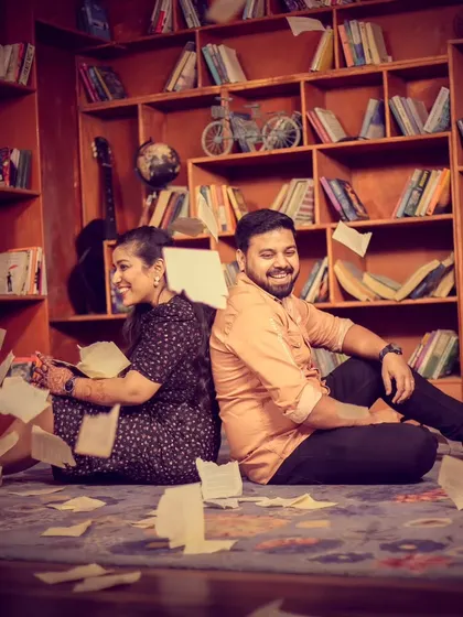 A fun, creative shot in a library-themed set. The couple is surrounded by flying pages, creating a dynamic and whimsical pre-wedding photograph.