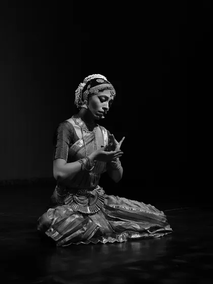 A seated pose in black and white, conveying a mood of quiet introspection. The hand mudra suggests the act of holding or contemplating something precious.