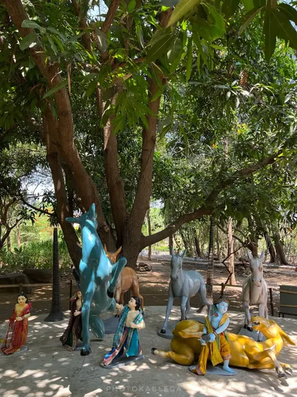 A collection of colorful statues depicting Krishna and his companions with animals under a large tree.