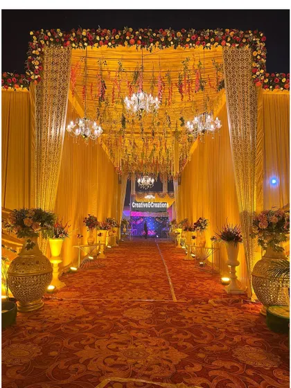 A grand entrance featuring a ceiling of hanging flowers and multiple chandeliers. The warm yellow and orange tones create a welcoming and luxurious atmosphere.