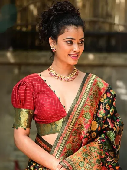 A model wears a red checked blouse with puff sleeves, accessorized with a simple gold choker that adds a touch of shine.