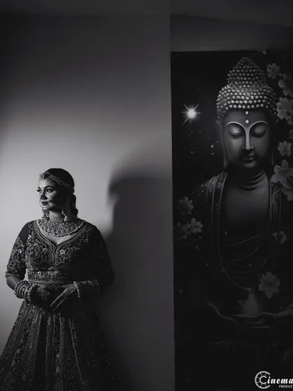 A serene black and white portrait of the bride standing beside a Buddha painting, creating a calm and spiritual atmosphere.