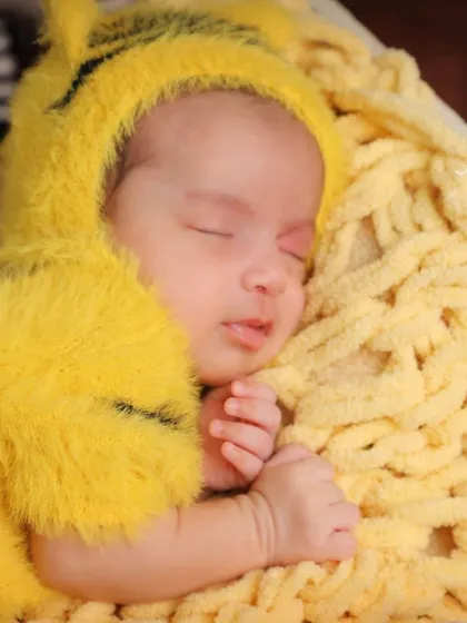 A close-up of our little tiger cub. You can see his tiny fingers and peaceful expression as he sleeps, cozy in his yellow outfit.