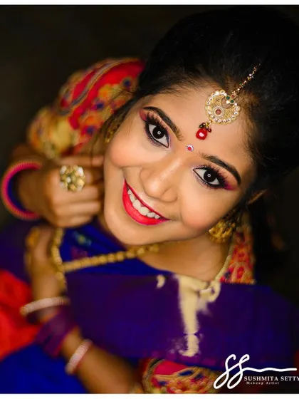 A joyful, top-angle shot that captures the complete bridal look, from the maang tikka to the radiant smile. The eye makeup is sharp and the lip color pops beautifully.