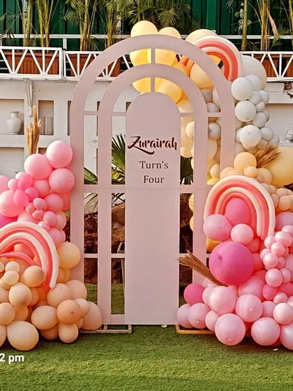 A modern and stylish boho rainbow theme for a 4th birthday. This outdoor setup uses arched backdrops and pastel balloon arrangements in a beautiful pink and peach palette.