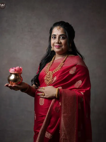 A close-up portrait in a red silk saree, capturing the expectant mother's serene expression as she holds a traditional pot, symbolizing prosperity and new beginnings.
