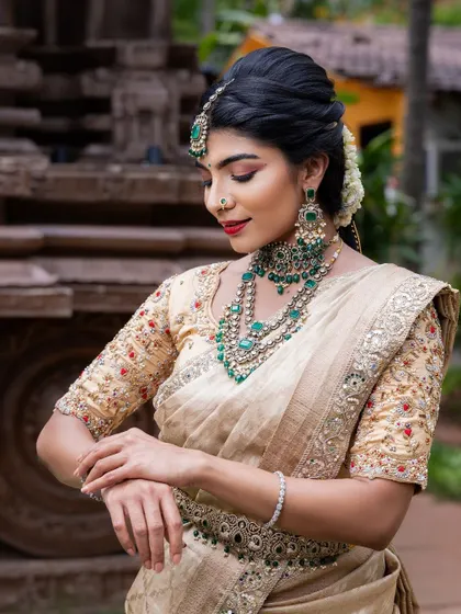 This elegant cream and gold tissue silk saree is paired with emerald jewelry for a stunning contrast. It's a sophisticated choice for a wedding reception or engagement, offering a regal and timeless appeal.